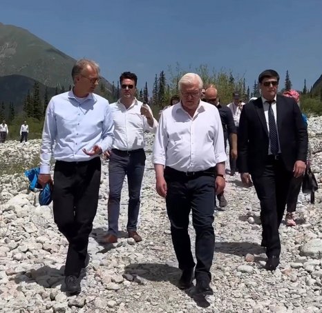 Eine Gruppe Männer wandert in Anzughosen und Hemd durch eine trockene, steinige Hochgebirgslandschaft.
