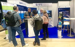 Eiin Messestand mit Bildschirmen, Postern und mehreren Besuchern.