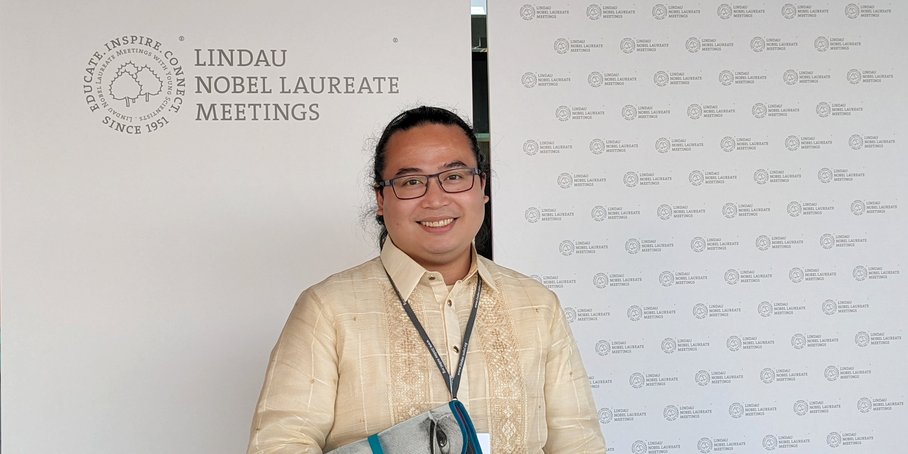 Jeffrey Perez steht vor dem Logo der Tagung