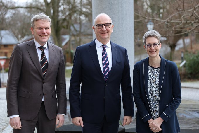 Three Persons standing in front of the stone columns.