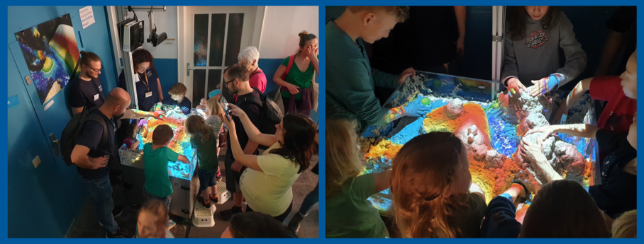 Menschen stehen um eine Sandbox und formen Berge aus Sand. Darauf werden buntes Licht und Höhenlinien rojiziert.