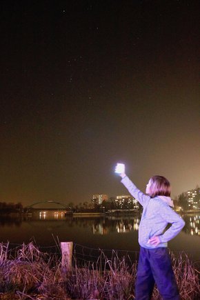 Ein Mensch steht mit Smartphone in der Hand und vergleicht das Bildschirmbild mit dem Sternenhimmel.