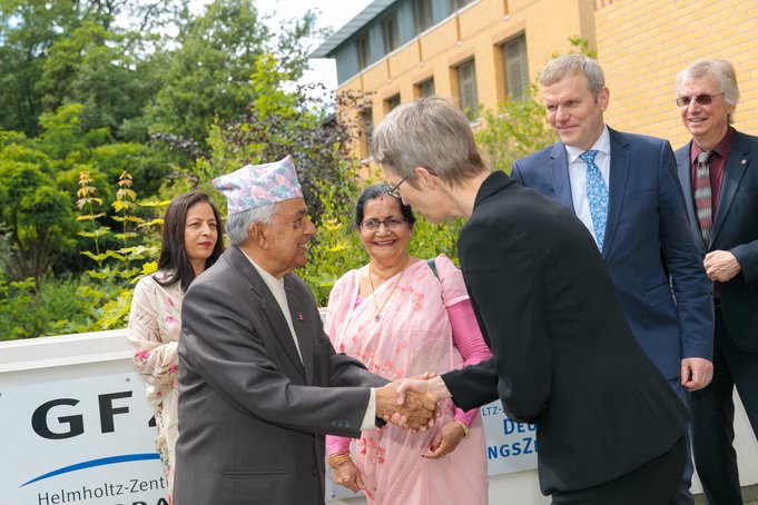 A man shakes the hand of a woman. Other people are standing next to him.