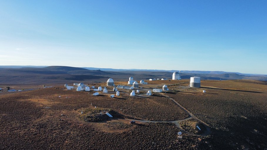African landscape with blue sky; the domes of the SAGOS observatory can be seen in the distance.