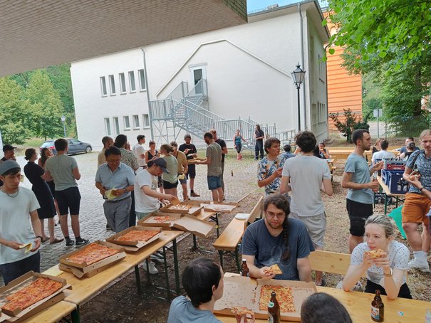 Menschen sitzen draußen an Tischen und essen Pizza