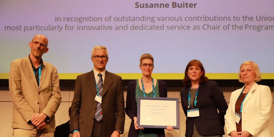 5 Personen auf der EGU vor einem Bildschirm. Frau Buiter hält den Preis (Urkunde in Rahmen)