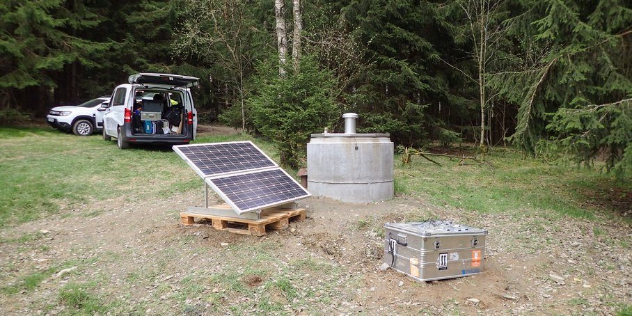 Photo: In a clearing in the forest, there is a borehole covered with a concrete lid. Next to it are measuring instruments and a solar station.